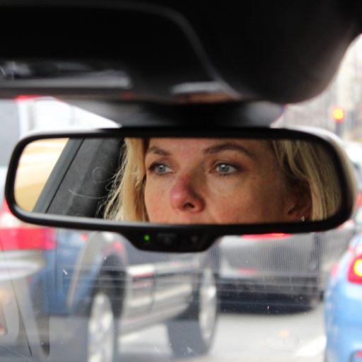 The eyes and nose of a woman with blonde hair photographed in the rear view mirror of a vehicle in traffic.