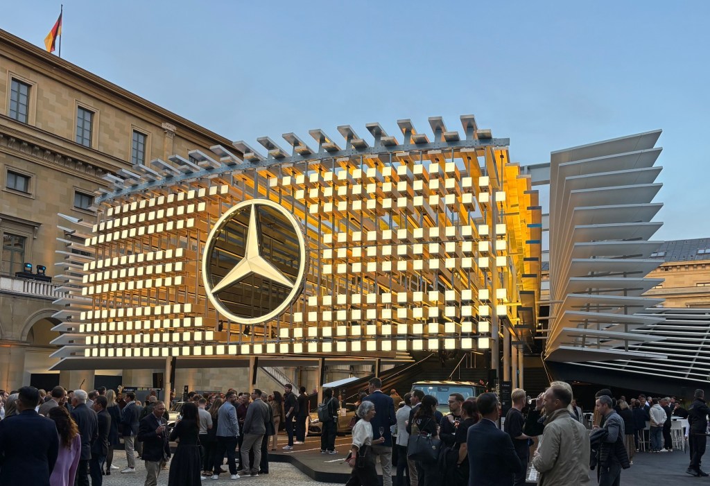 A giant 3D recreation of the new illuminated Mercedes-Benz grille above the entrance to an outdoor exhibit.